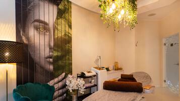 A modern bedroom with a large mural, a green chair, a bed with brown pillows, a desk with a lamp, and a hanging plant.