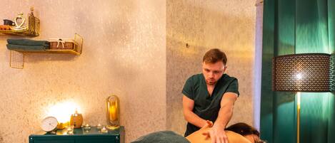 A massage therapy room with a massage table, a clock, and a small shelf with items.