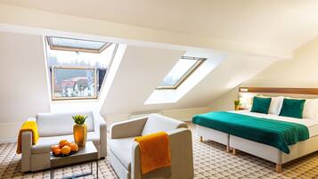 A modern, well-lit room with a bed, two sofas, a coffee table, and a small table with oranges and a pineapple.