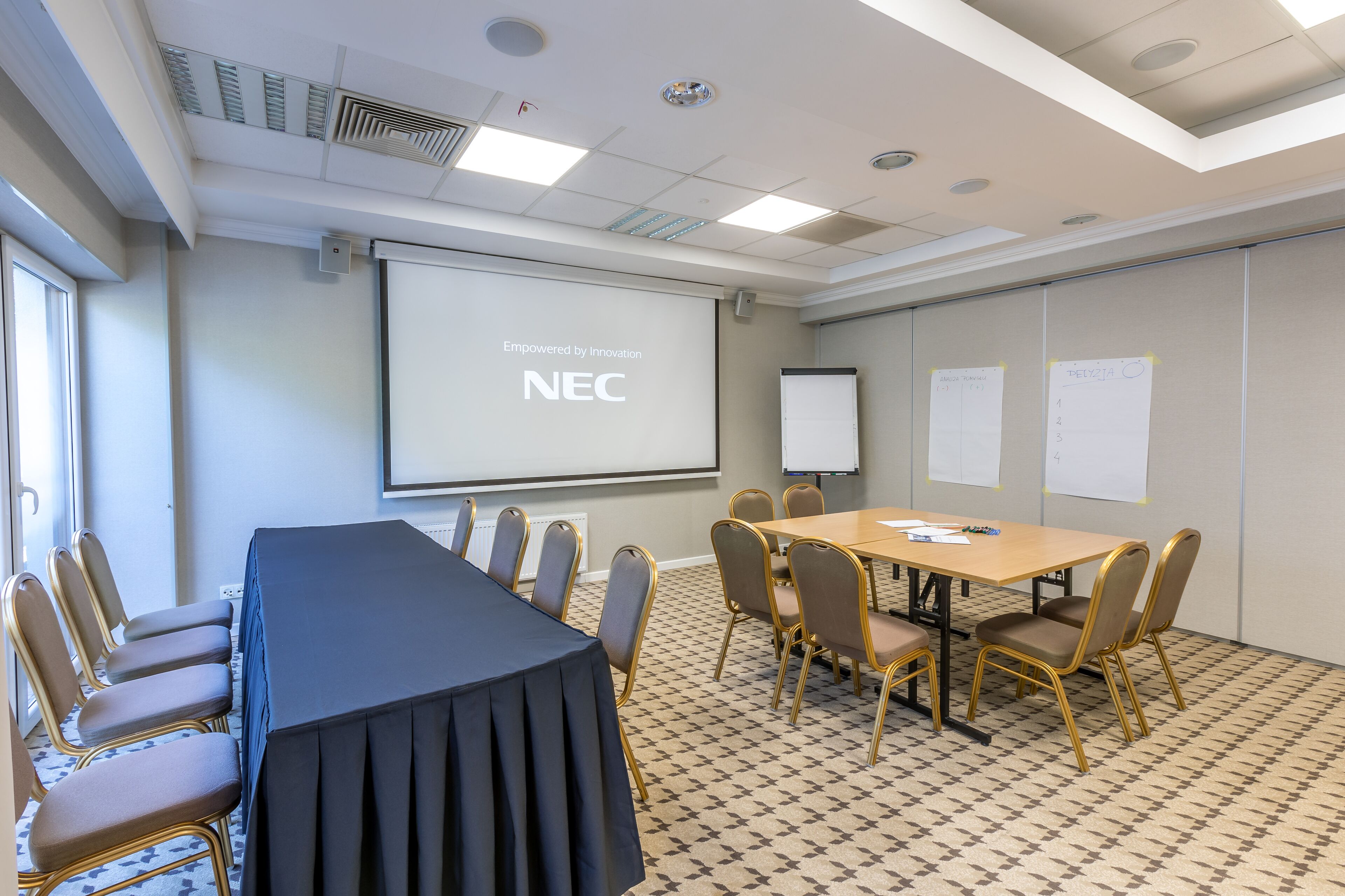 A conference room with a long table, chairs, a projector screen, and whiteboards.