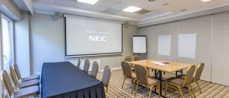A conference room with a long table, chairs, a projector screen, and whiteboards.