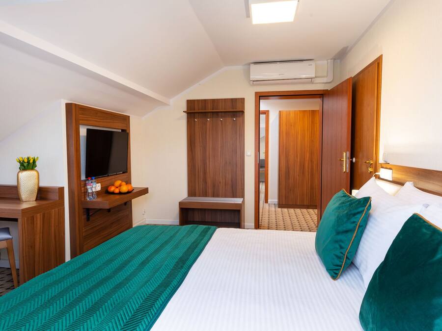 Quarto de hotel com cama, escrivaninha, televisão, guarda-roupa e ar condicionado.