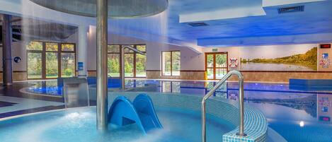 Una amplia piscina interior con un elemento acuático central, señalización clara y vistas al exterior a través de grandes ventanales.