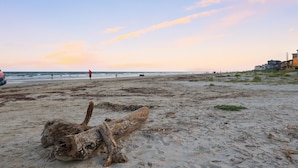 A beach with a large log in the foreground, a distant person in red, and a building on the right. - Pelicans soar! Oean view and steps to the beach. Remodeled & pet friendly too. (Galveston)
