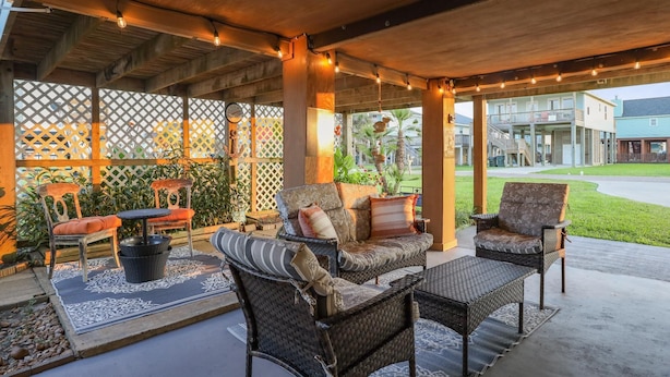 An outdoor patio area with wicker furniture, a table, and chairs. There are plants and a wooden fence in the background. - Pelicans soar! Oean view and steps to the beach. Remodeled & pet friendly too. (Galveston)
