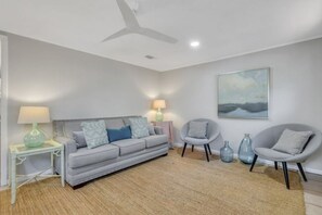 A modern living room with a grey sofa, two armchairs, a small side table, and a ceiling fan.