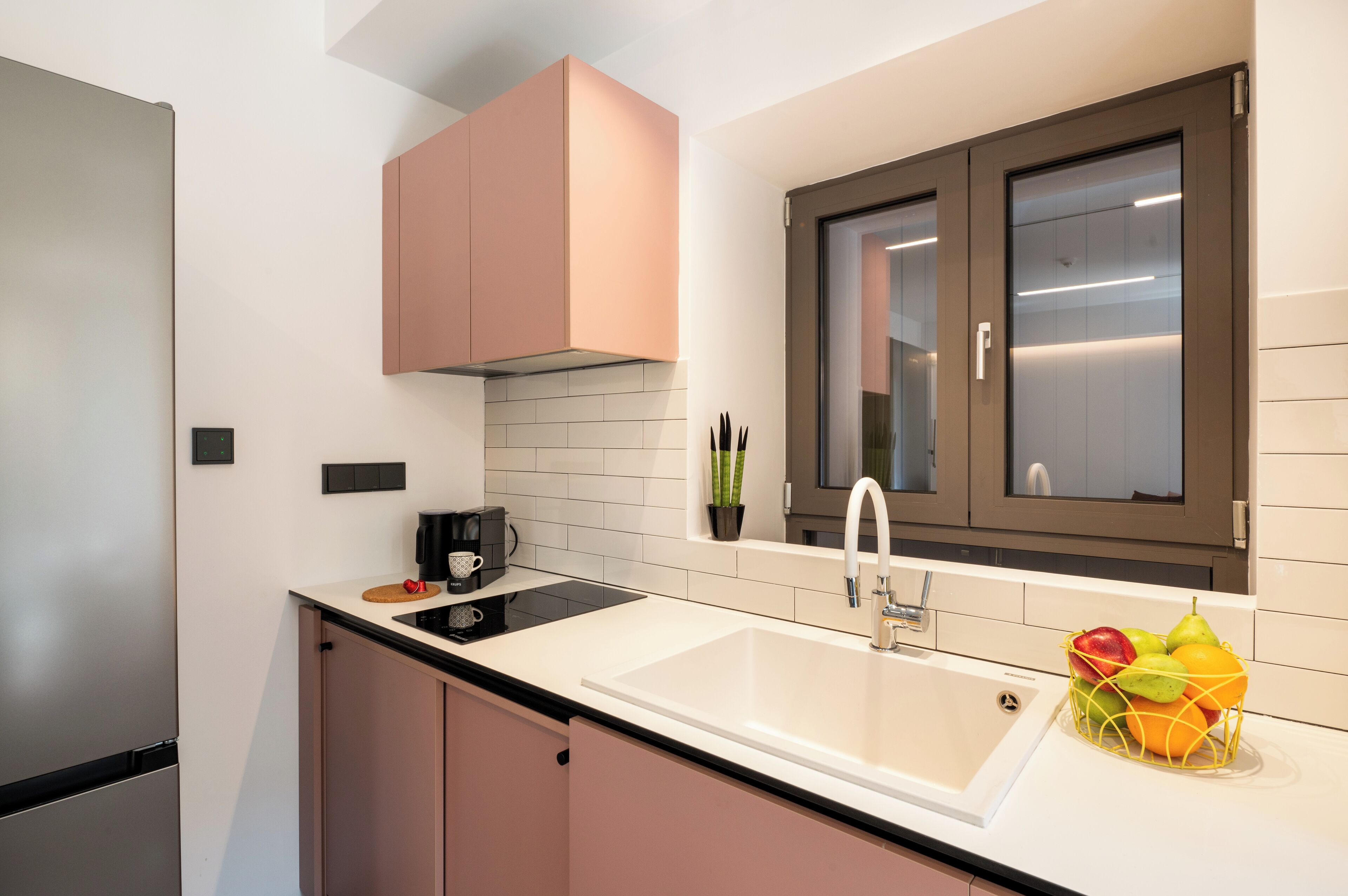 A modern kitchen with a white sink, stainless steel refrigerator, and pink cabinets.