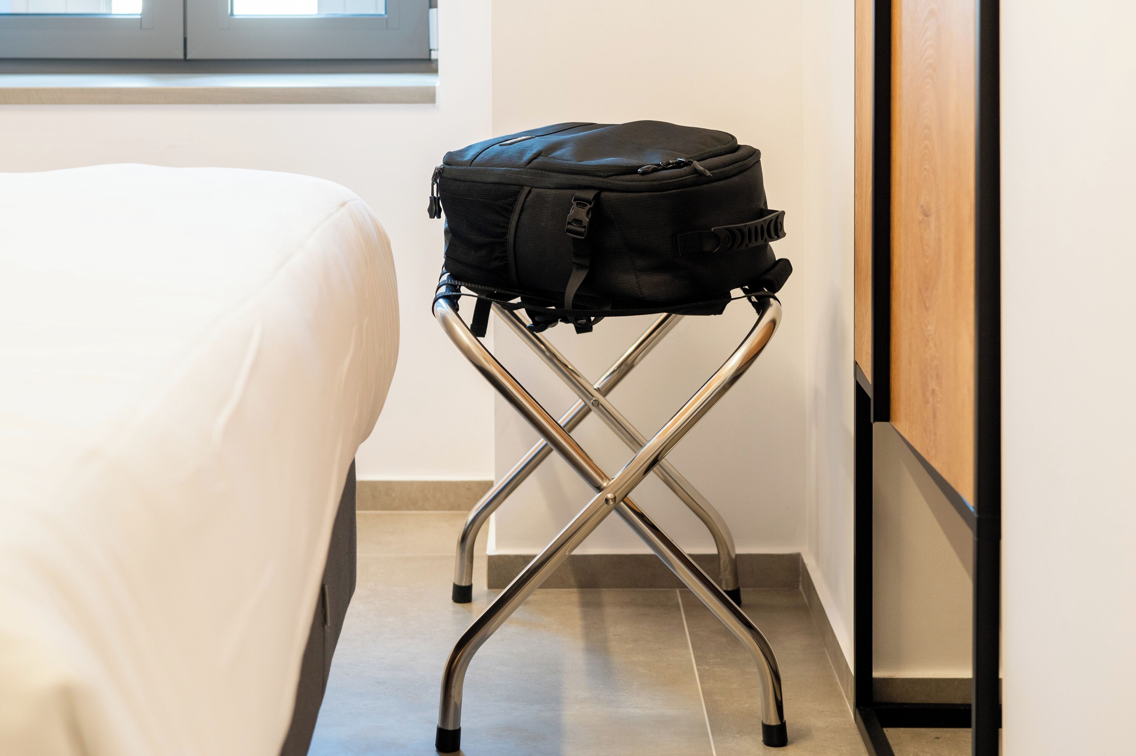 Een zwarte rugzak op een metalen klapstoel in een hotelkamer.