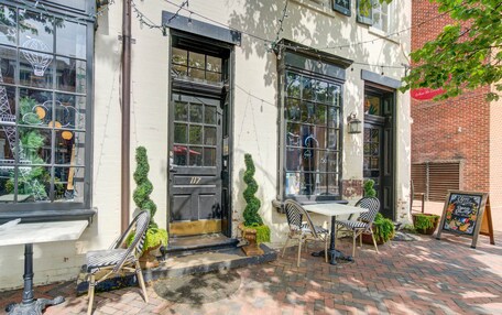 An outdoor seating area with tables and chairs, a brick pathway, and a building with large windows and a door.