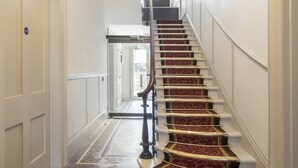 A grand staircase with ornate carpet and a mosaic floor, leading to a hallway with doors.