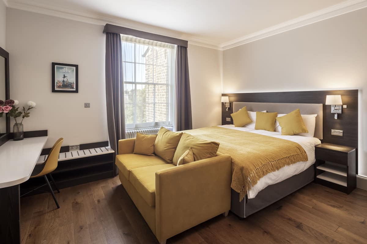 A hotel room with a bed, a sofa, a desk, and a window with curtains.