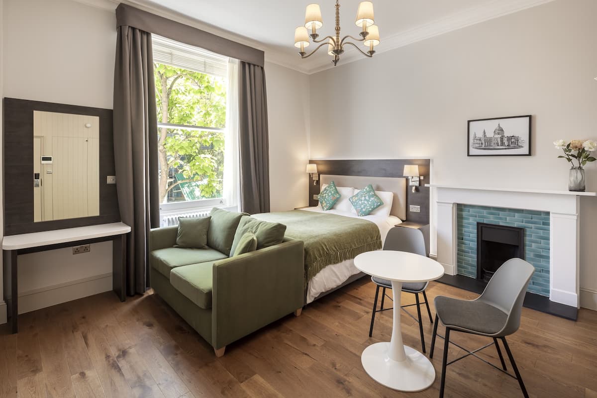 A modern bedroom with a bed, a sofa, a dining table, and a fireplace.