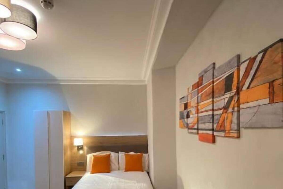 A hotel room with a bed, a nightstand, a lamp, a radiator, and a wall art piece.