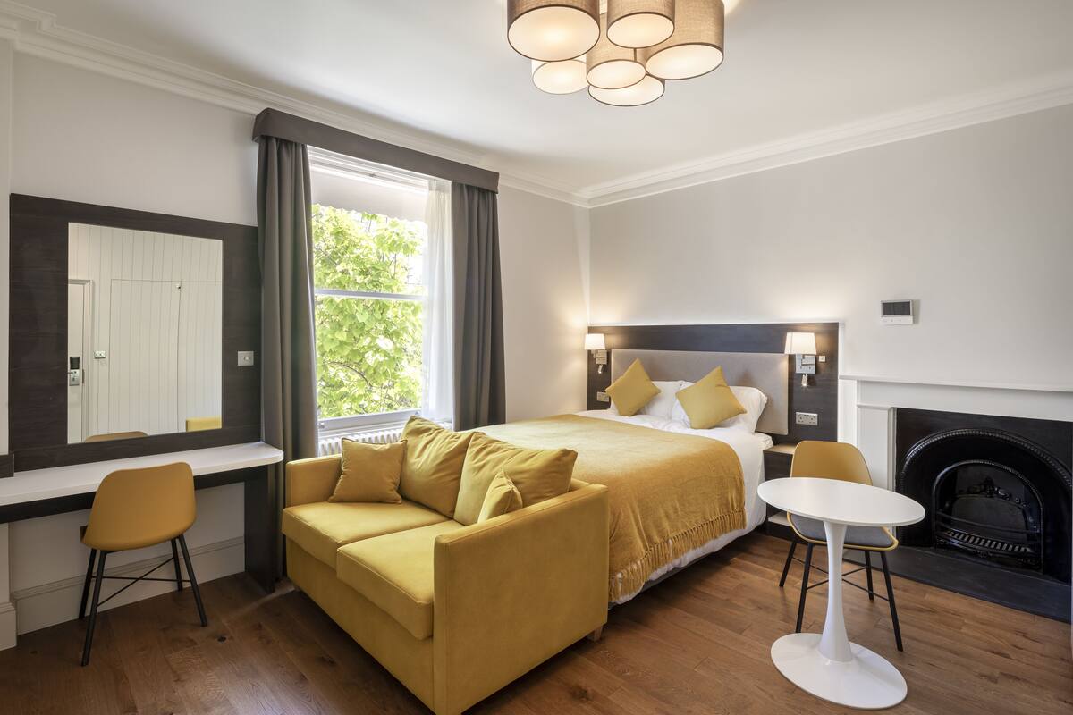 A modern hotel room with a bed, a sofa, a small table, and a fireplace.