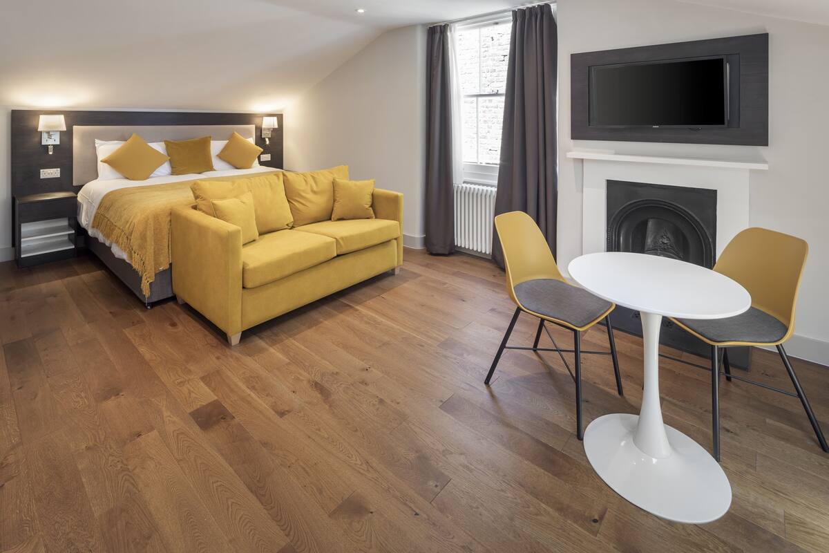 A modern hotel room with a bed, a sofa, a TV, and a fireplace.
