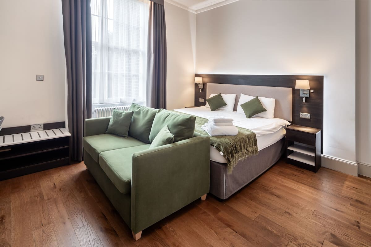 A modern hotel room with a green sofa, a bed with white linens, and a wooden floor.