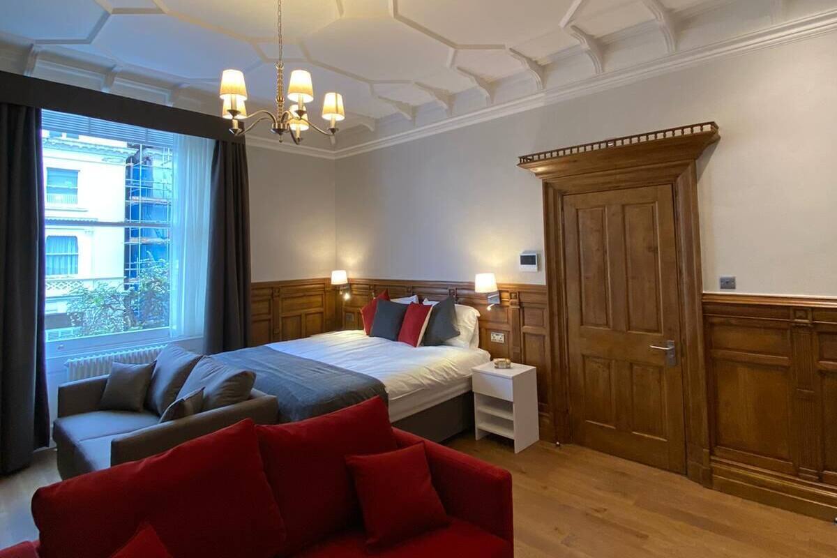 A bedroom with a large bed, a red sofa, wooden wardrobe, and a window with curtains.