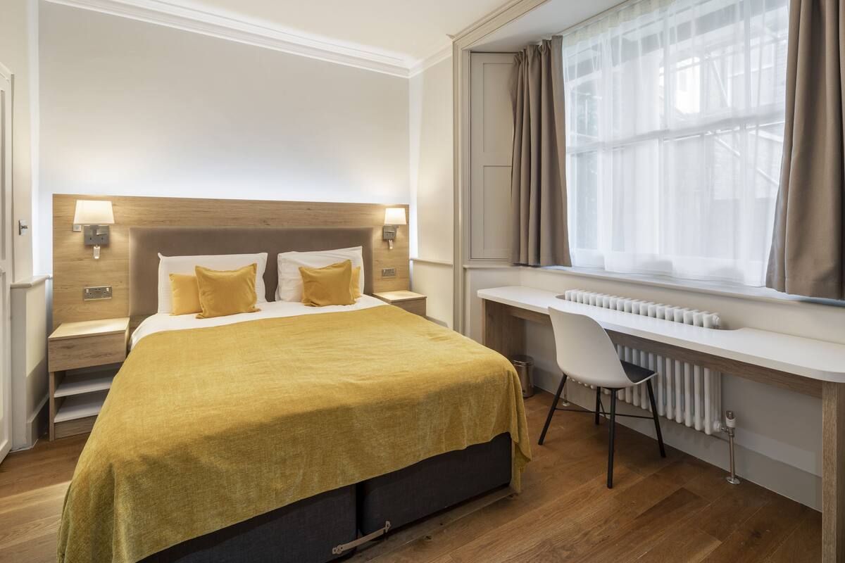 A modern hotel room with a bed, bedside tables, a desk, and a chair.