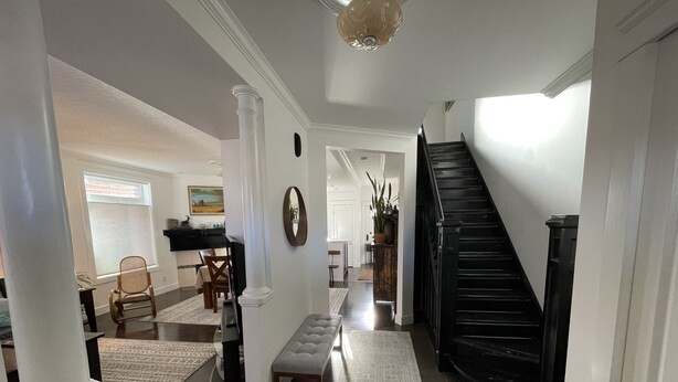 Un pasillo espacioso con una escalera negra, un comedor con sillas y una mesa, y una sala de estar con sofá y mesa de centro.