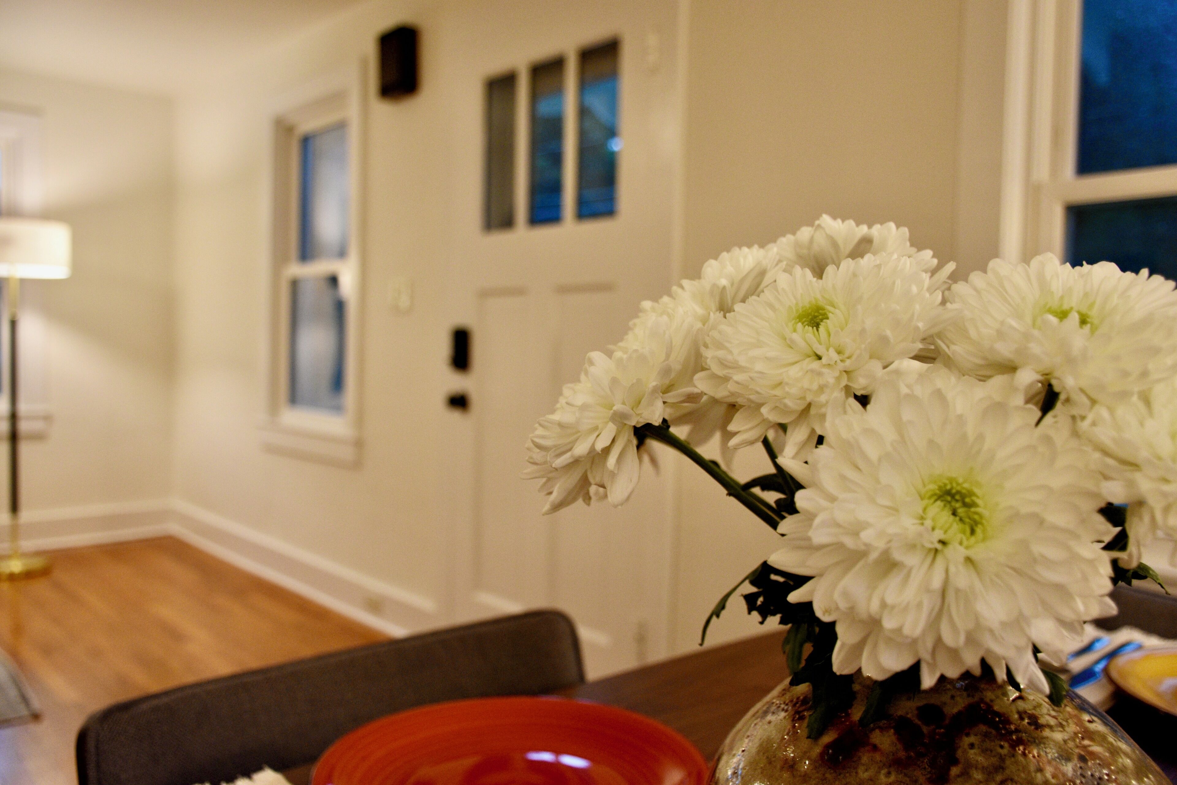 A dining area with a table set for two, a vase with white flowers, and a red bowl.