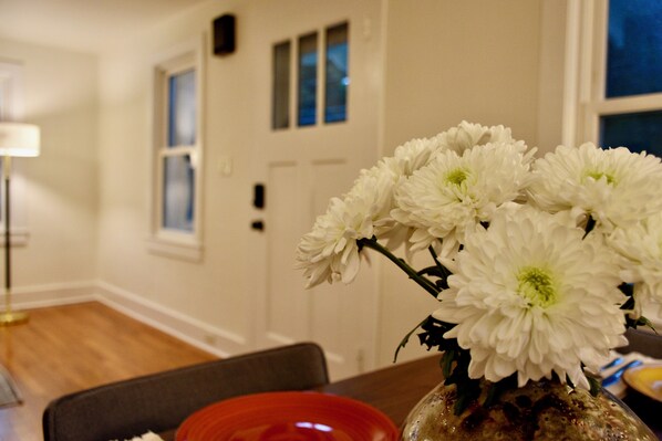 A dining area with a table set for two, a vase with white flowers, and a red bowl.