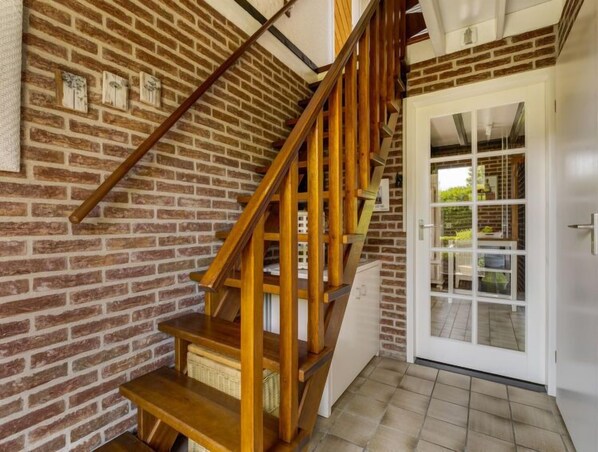 A wooden staircase with a brick wall background, a white door with glass panels, and a tiled floor. - Haus Anni by Interhome (Wolphaartsdijk)