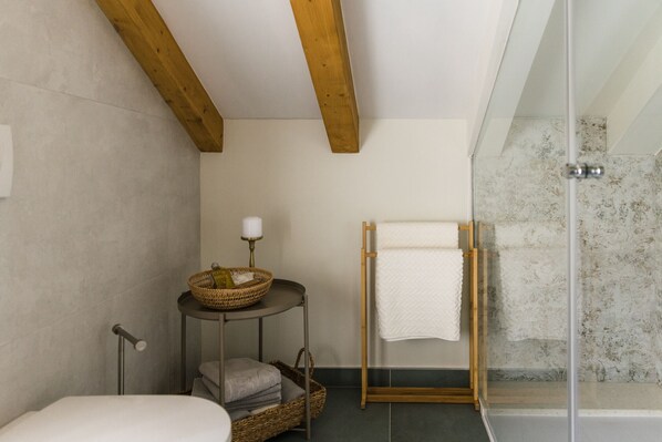 Un baño con bañera, cabina de ducha de cristal, viga de techo de madera, perchero y una pequeña mesa con cesta y vela.