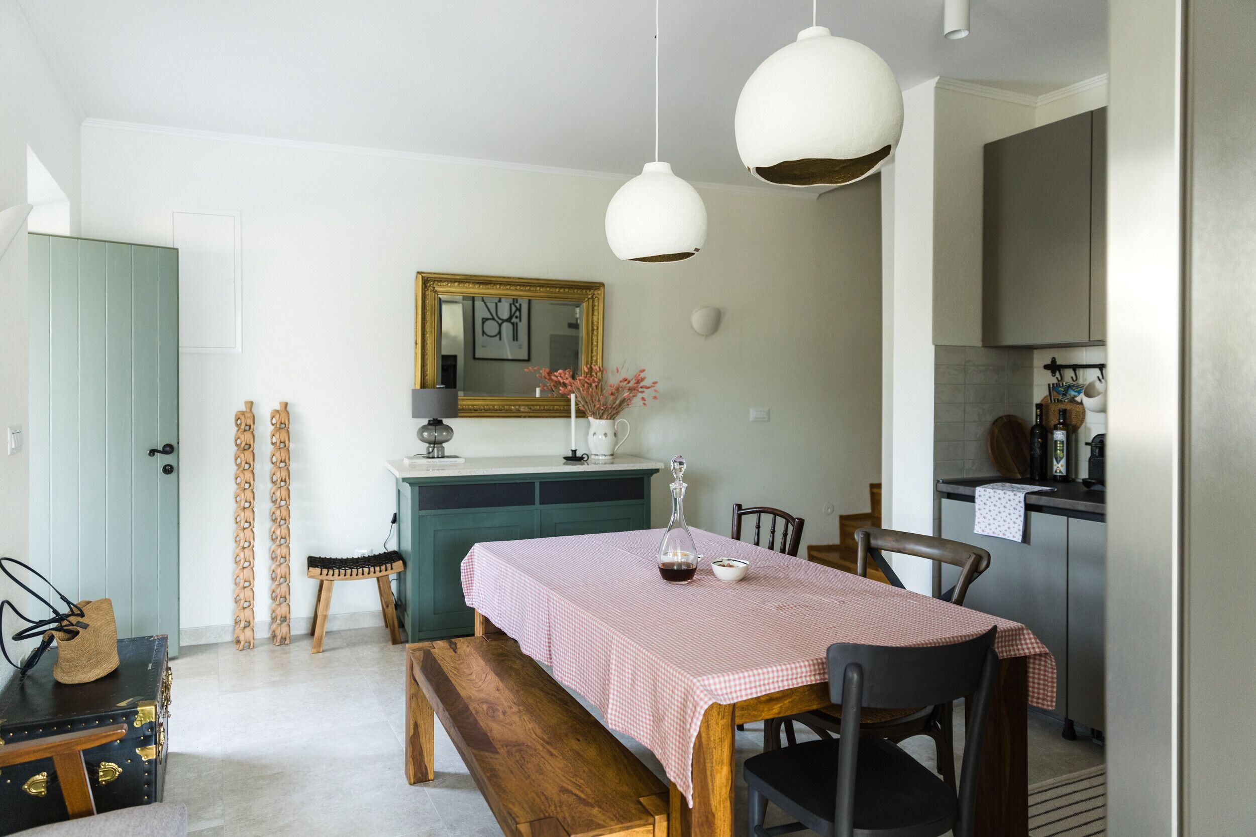 Un comedor con una mesa preparada para dos personas, un banco y una cocina al fondo.