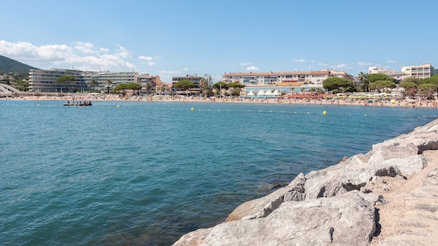 A coastal area with a rocky shoreline, a beach with people, and buildings in the background. - T2 with balcony close to the sea. (Sainte-Maxime)