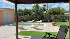 Ein überdachter Außenbereich mit Schwimmbad, Liegestühlen und einer Pergola.