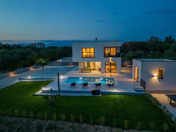 A modern two-story house with a swimming pool, outdoor seating, and a well-maintained lawn.