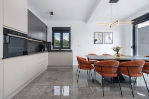 A modern kitchen with a built-in oven, a coffee machine, and a dining area with a table and chairs.