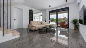 A modern living room with a beige sofa, a brown armchair, and two coffee tables. - Villa Rocinante (Policnik)