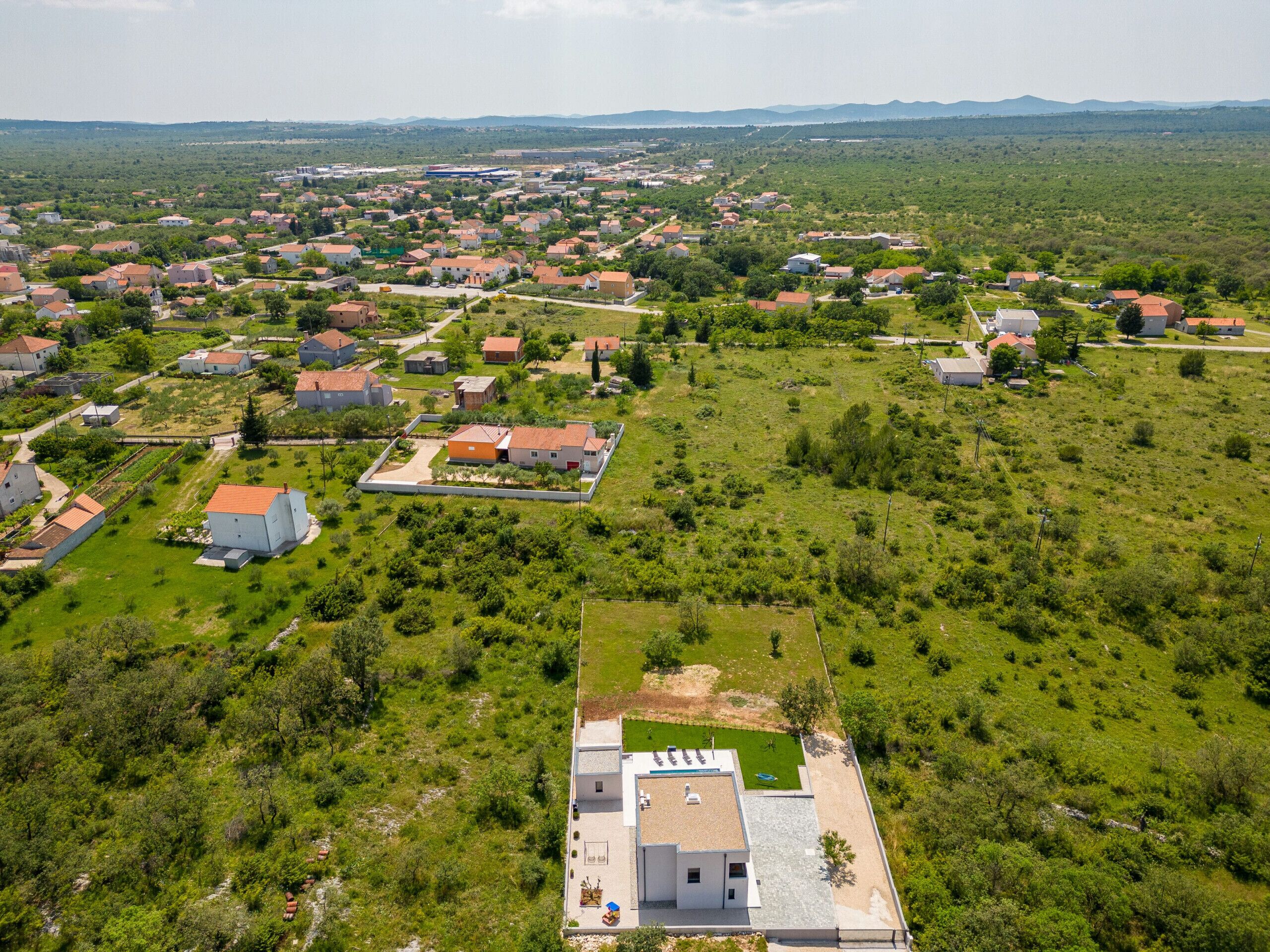 An aerial view of a residential area with houses, green spaces, and a large open field.