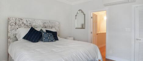 Un dormitorio con una cama grande, ropa de cama blanca, un cabecero estampado y un tapete azul y negro.