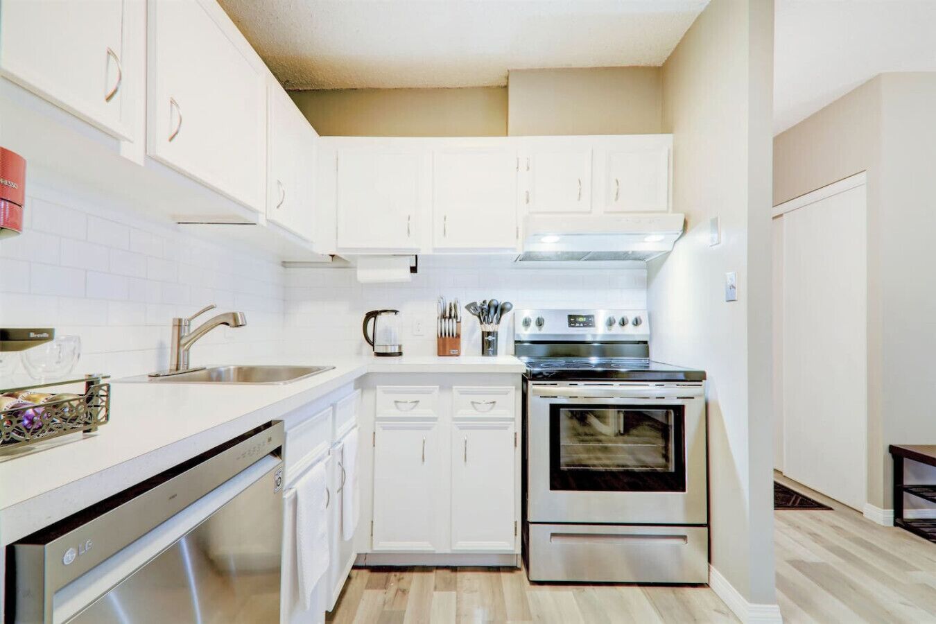 A compact kitchen with white cabinets, a stainless steel stove, and a dishwasher.