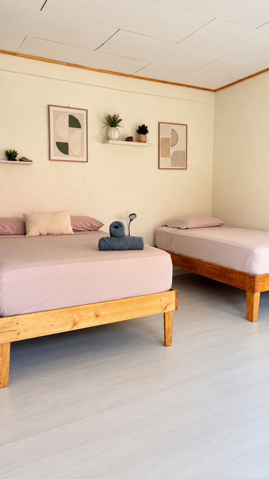 Une chambre à coucher avec deux lits en bois, des murs de couleur claire et un plafond doté d’un éclairage encastré.