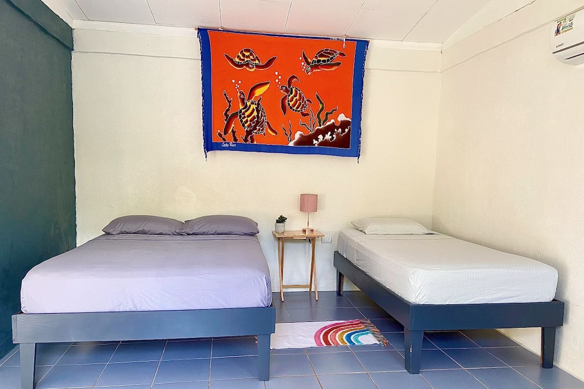 A bedroom with two beds, a small table, a lamp, and a colorful rug.