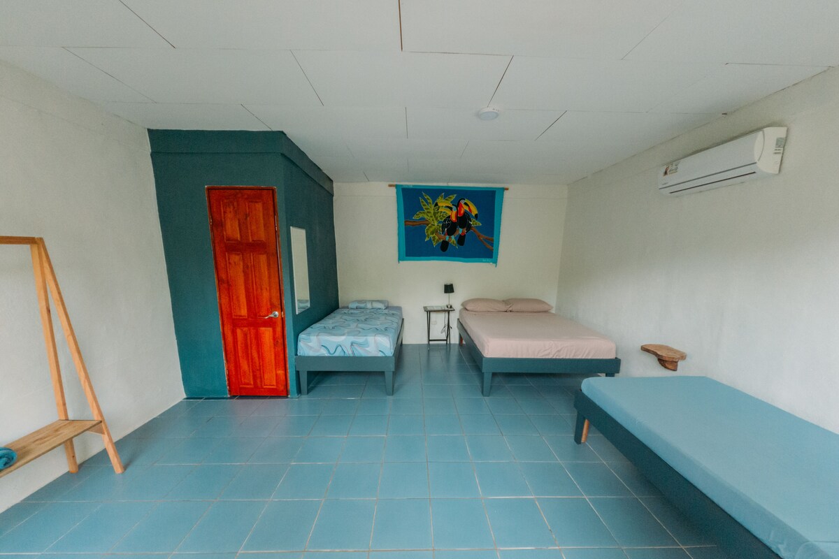 A room with two beds, a red door, a blue wall, and a painting.