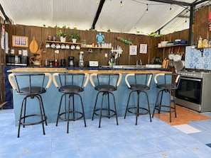 Zona de bar con cuatro taburetes, cocina con estufa y diferentes utensilios de cocina y adornos en la pared.