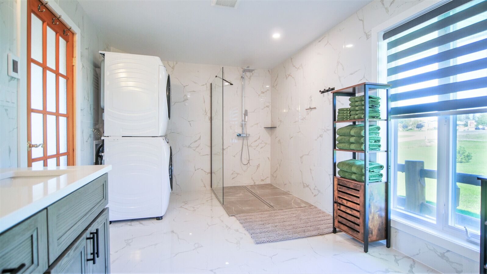 Une salle de bain avec une douche en verre, un sol en marbre blanc et un meuble en bois contenant des serviettes.