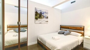 A bedroom with a wooden headboard, white bedding, a painting of a mountain landscape, and a bedside table with a lamp. - Chic DT Suite at Stampede w/ Free Parking, AC (Calgary)