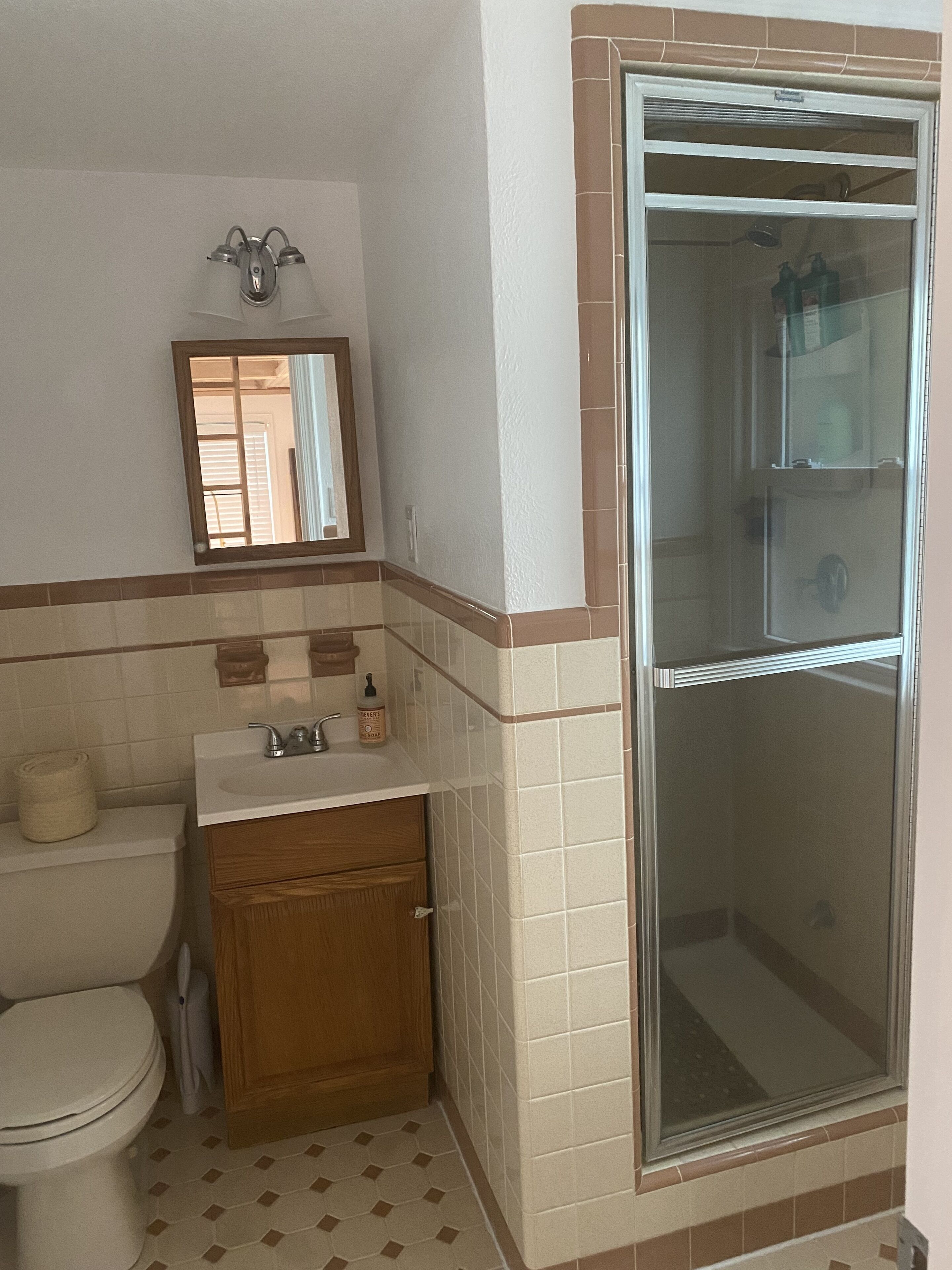 A bathroom with a toilet, sink, mirror, and shower enclosure.