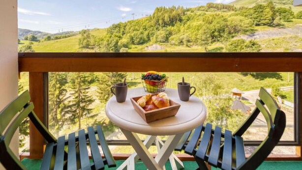 Varanda com mesa e duas cadeiras, com vista para uma paisagem verdejante com colinas e árvores.