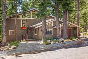 A modern two-story house with a front porch, surrounded by trees and a gravel driveway.