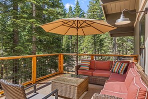 A covered outdoor seating area with a cushioned sofa, a wicker table, and a large umbrella. - Mountain Dream in Homewood - Chamberlands (Homewood)