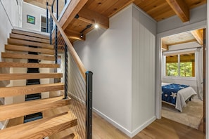 A staircase with wooden steps and metal railings, leading to a room with a bed and a window.