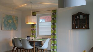 Un coin repas avec une table et des chaises, une carte accrochée au mur, une fenêtre avec des stores et un meuble.
