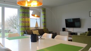 Un salon moderne comprenant un coin repas, un canapé, un téléviseur et une grande fenêtre avec des rideaux.