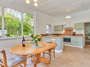 Une cuisine moderne dotée d’un îlot central, de grandes fenêtres et d’un coin repas avec une table et des chaises en bois.